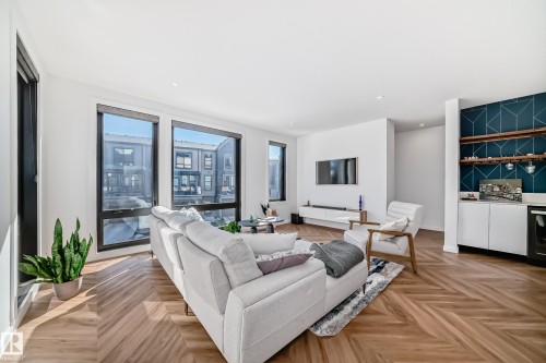 Open-concept living space with herringbone wood-finish flooring, recessed lighting, and large windows with dark trim - 46 1304 Rutherford Road, Edmonton, AB - Indoor Photo Showing Living Room
