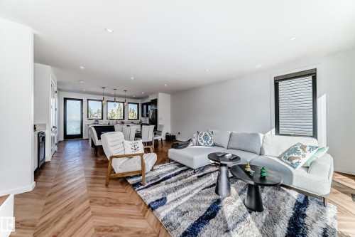 Bright living area featuring wood-finish flooring with a herringbone pattern, recessed lighting, and a large window with privacy blinds - 46 1304 Rutherford Road, Edmonton, AB - Indoor Photo Showing Living Room