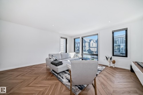 Spacious living area featuring chevron wood-finish flooring, recessed lighting, and multiple large windows with black trim - 46 1304 Rutherford Road, Edmonton, AB - Indoor Photo Showing Living Room