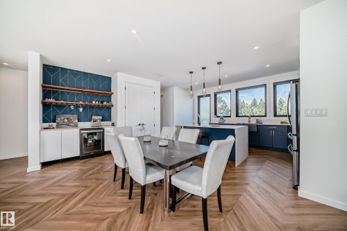Open-concept living space featuring herringbone wood-finish flooring, a built-in beverage bar with open shelving, and a kitchen island with pendant lighting - 46 1304 Rutherford Road, Edmonton, AB - Indoor Photo Showing Dining Room