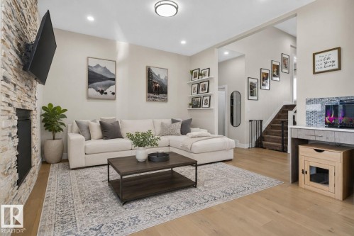 Spacious living area featuring light wood-finish flooring, a stacked stone fireplace surround, recessed lighting, and a neutral color palette - 4204 55Av, Lamont, AB 