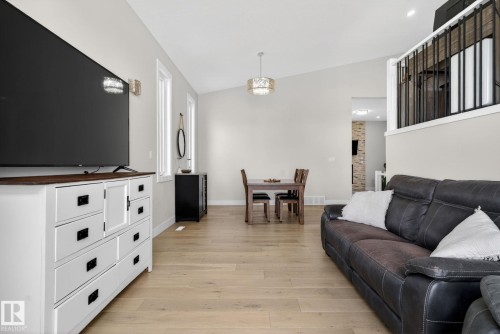 Open-concept living space featuring vaulted ceilings, light wood-finish flooring, a contemporary chandelier, and a black wrought iron railing - 4204 55Av, Lamont, AB 