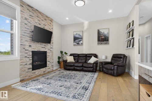 Living area featuring a floor-to-ceiling stacked stone fireplace, a large picture window, recessed lighting, wood-finish flooring, and built-in floating shelves - 4204 55Av, Lamont, AB 