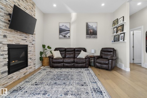 Living area featuring a floor-to-ceiling stacked stone fireplace with a black insert, recessed lighting, wood-finish flooring, and white baseboards - 4204 55Av, Lamont, AB 