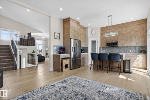 Open-concept kitchen featuring wood-finish cabinetry, stainless steel appliances, a tiled backsplash, and an island with seating - 4204 55Av, Lamont, AB 