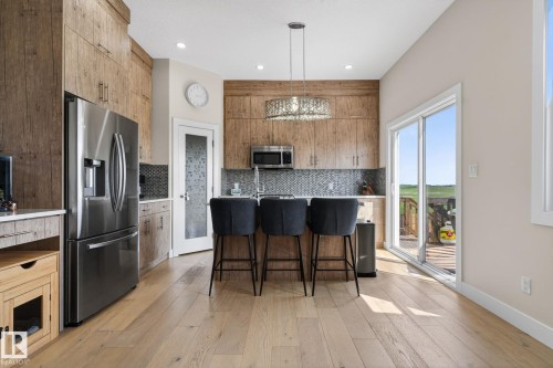 Kitchen featuring wood-finish cabinetry, stainless steel appliances, a mosaic tile backsplash, a central island with bar seating, and wood-finish flooring - 4204 55Av, Lamont, AB 