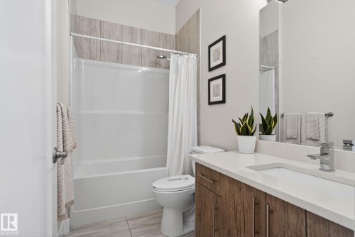 Bathroom featuring a white tub/shower combination with a textured tile surround, a built-in vanity with wood-finish cabinetry, a light-toned countertop, and an integrated rectangular sink - 4204 55Av, Lamont, AB 