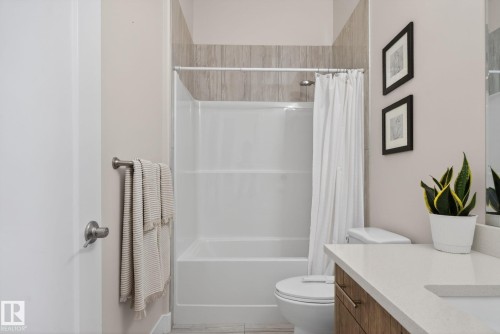 Bathroom featuring a white shower/tub combination with tiled surround, a toilet, and a vanity with a light-toned countertop - 4204 55Av, Lamont, AB 