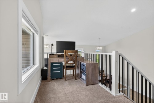 Open loft space featuring plush carpeting, a large window, white painted walls, white trim, and a white railing with black metal balusters - 4204 55Av, Lamont, AB 