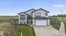 Contemporary two-story residence featuring light-colored siding with dark trim accents, a prominent front-facing two-car garage, multiple large windows, a well-maintained lawn, and a concrete driveway - 4204 55Av, Lamont, AB 
