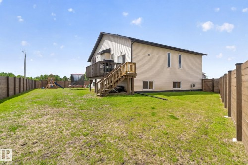 Expansive backyard featuring a wood-toned privacy fence, a raised wooden deck with staircase access, and a cream-colored exterior with multiple windows - 4204 55Av, Lamont, AB 