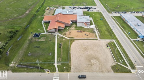 Spacious property featuring a large building with a terracotta-toned roof, multiple paved parking areas, extensive grassy fields, and two distinct playground structures - 4204 55Av, Lamont, AB 