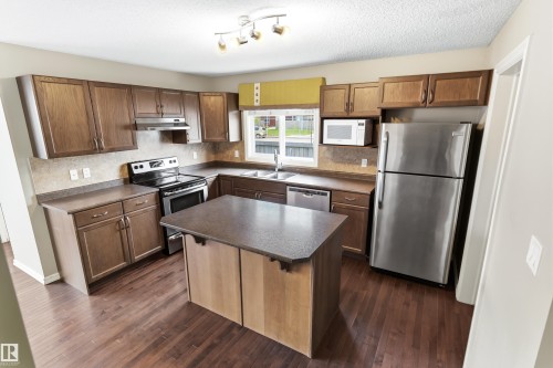 Open-concept kitchen featuring wood-finish flooring, dark wood cabinetry, a central island, stainless steel appliances, and a window with natural light - 8204 180 Avenue, Edmonton, AB 