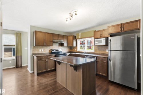 Kitchen featuring wood-finish flooring, dark wood cabinetry, a central island, a stainless steel refrigerator, and a built-in microwave - 8204 180 Avenue, Edmonton, AB 