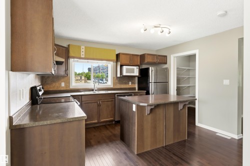 Kitchen featuring rich wood-finish flooring, a central island with a contrasting countertop, stainless steel appliances, ample cabinetry, and a pantry with built-in shelving - 8204 180 Avenue, Edmonton, AB 