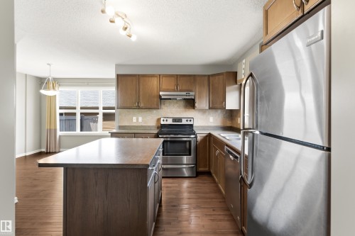 Kitchen featuring wood-finish flooring, stainless steel appliances, wood cabinetry, a central island, and track lighting - 8204 180 Avenue, Edmonton, AB 