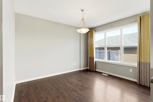 Spacious room featuring rich wood-finish flooring, a multi-pane window, neutral wall tones, and a suspended ceiling light fixture - 8204 180 Avenue, Edmonton, AB 