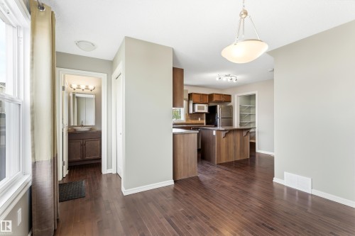 Open-concept living space featuring wood-finish flooring, a kitchen island with seating, dark wood cabinetry, and a visible pantry - 8204 180 Avenue, Edmonton, AB 