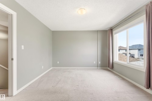 Spacious room featuring light-toned carpeting, a broad window with white trim, and a semi-flush mount ceiling light fixture - 8204 180 Avenue, Edmonton, AB 