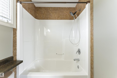 Bathtub and shower combination featuring a white acrylic surround, chrome fixtures, a handheld showerhead, and a bronze-toned shower curtain rod - 8204 180 Avenue, Edmonton, AB 