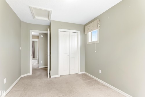 Carpeted room featuring a white interior door, a bi-fold closet with panel detailing, a window with a valance, and a ceiling access panel - 8204 180 Avenue, Edmonton, AB 