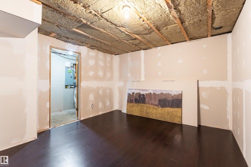 Space featuring dark wood-finish flooring, drywall-ready walls, and exposed ceiling joists with insulation - 8204 180 Avenue, Edmonton, AB 