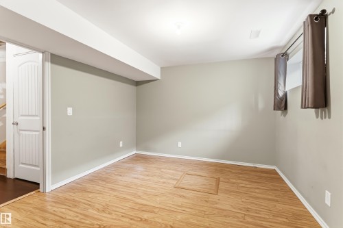 Spacious room featuring wood-finish flooring, light grey walls, white trim, and a white interior door - 8204 180 Avenue, Edmonton, AB 