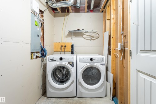 Dedicated utility area featuring a washer and dryer hookup, exposed ceiling joists and ductwork, panel-style interior door, and drywall-ready walls - 8204 180 Avenue, Edmonton, AB 