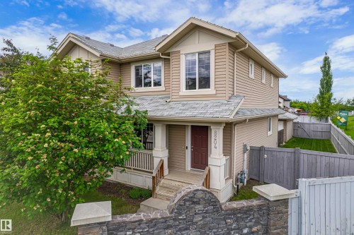 Two-story residence featuring light-colored siding, a covered front porch with railings, and a stone-faced retaining wall - 8204 180 Avenue, Edmonton, AB 