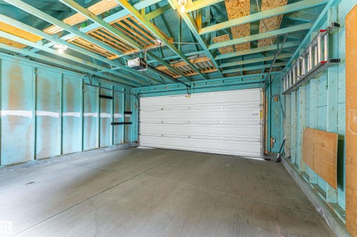 Garage interior featuring a concrete floor, exposed ceiling joists, and a white overhead garage door - 8204 180 Avenue, Edmonton, AB 