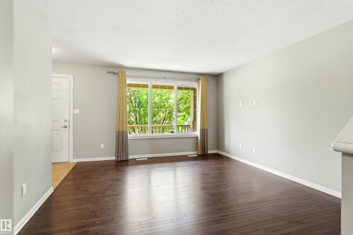 Spacious room featuring wood-finish flooring, a large window with a natural backdrop, light grey walls, white trim, and a textured white ceiling - 8204 180 Avenue, Edmonton, AB 