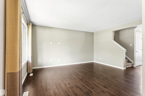 Spacious room featuring wood-finish flooring, light neutral wall tones, and white baseboards - 8204 180 Avenue, Edmonton, AB 