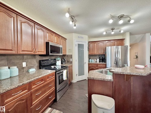 Spacious kitchen featuring warm wood cabinetry, granite countertops, tile backsplash, and stainless steel appliances - 105 Greystone Crescent, Spruce Grove, AB 