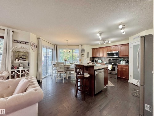Open-concept kitchen featuring wood-finish flooring, rich wood cabinetry, stainless steel appliances, and an eat-at island - 105 Greystone Crescent, Spruce Grove, AB 