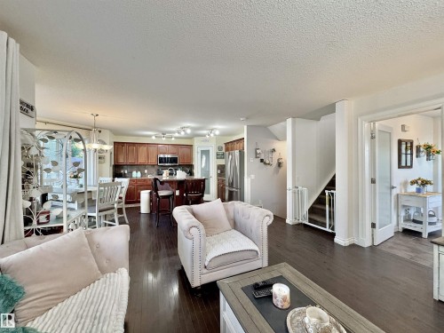 Open-concept living space featuring wood-finish flooring, a kitchen with rich wood cabinetry and stainless steel appliances, a dining area with a chandelier, and a stairway with white risers - 105 Greystone Crescent, Spruce Grove, AB 