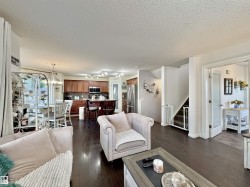 Open-concept living space featuring wood-finish flooring, a kitchen with rich wood cabinetry and stainless steel appliances, a dining area with a chandelier, and a stairway with white risers - 