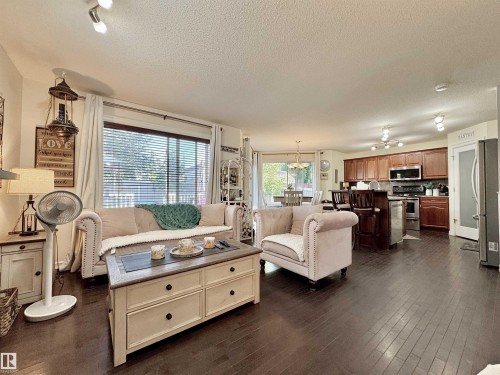 Open-concept living area featuring rich wood-finish flooring, track lighting, a full kitchen with dark wood cabinetry and stainless steel appliances, and a dining area with a chandelier - 105 Greystone Crescent, Spruce Grove, AB 