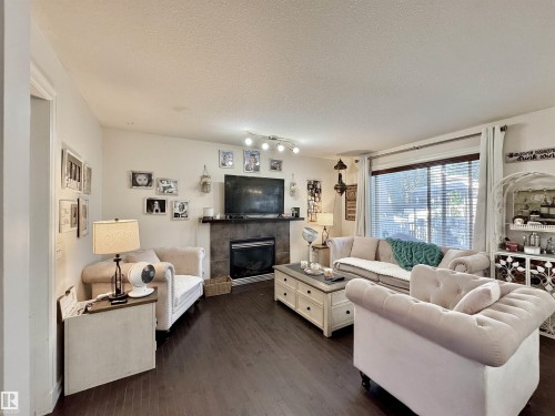 Spacious living area featuring dark wood-finish flooring, a contemporary fireplace with a stone surround, recessed lighting, and a large window with horizontal blinds - 105 Greystone Crescent, Spruce Grove, AB 
