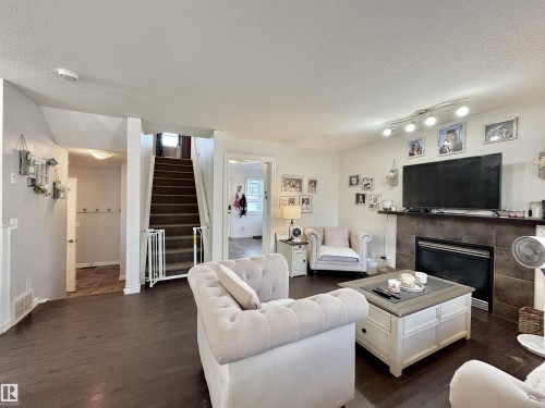 Living area featuring wood-finish flooring, a tiled fireplace with mantel, and a track lighting fixture - 105 Greystone Crescent, Spruce Grove, AB 