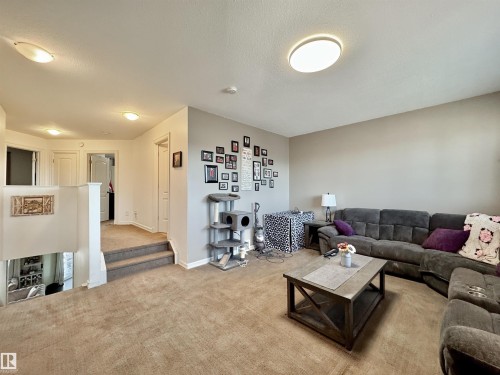 Carpeted living area featuring a neutral color palette, recessed and flush-mount ceiling lighting, and a partial view of a staircase and hallway with white trim and doors - 105 Greystone Crescent, Spruce Grove, AB 