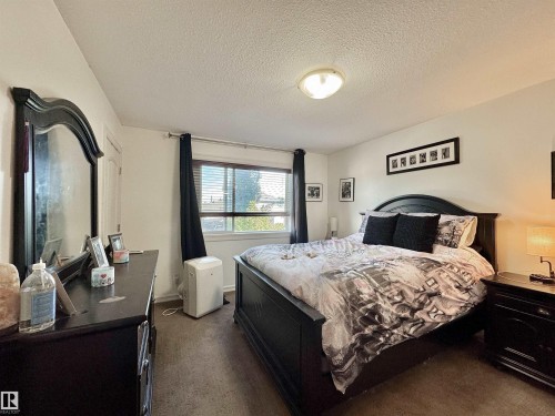 Carpeted bedroom featuring a large window with blinds, a built-in closet with a white door, and a flush-mount ceiling light fixture - 105 Greystone Crescent, Spruce Grove, AB 