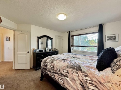 Bedroom featuring a large window with horizontal blinds, overhead ceiling light fixture, and brown carpeting - 105 Greystone Crescent, Spruce Grove, AB 