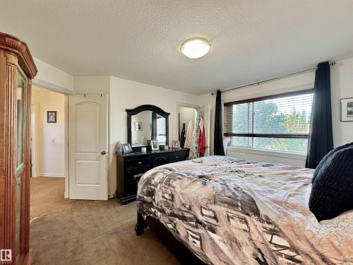Bedroom featuring a large window with blinds, a ceiling-mounted light fixture, and warm-toned carpeting - 105 Greystone Crescent, Spruce Grove, AB 