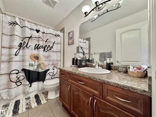 Bathroom featuring a vanity with wood-finish cabinetry, a white oval sink, and a speckled countertop - 105 Greystone Crescent, Spruce Grove, AB 