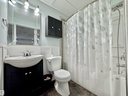 Bathroom featuring a dark wood-finish vanity with an integrated sink, a matching wall-mounted cabinet, a framed mirror with overhead lighting, a white toilet, and a combination tub/shower with a curved curtain rod - 105 Greystone Crescent, Spruce Grove, AB 