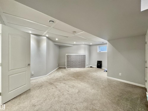 Spacious room featuring light gray walls, plush carpeting, a white paneled door, recessed lighting, and a window providing natural light - 105 Greystone Crescent, Spruce Grove, AB 