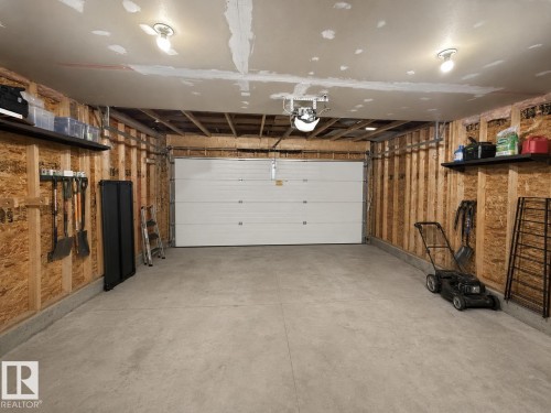 Spacious garage featuring a concrete floor, exposed wood stud walls, and a white overhead door - 105 Greystone Crescent, Spruce Grove, AB 