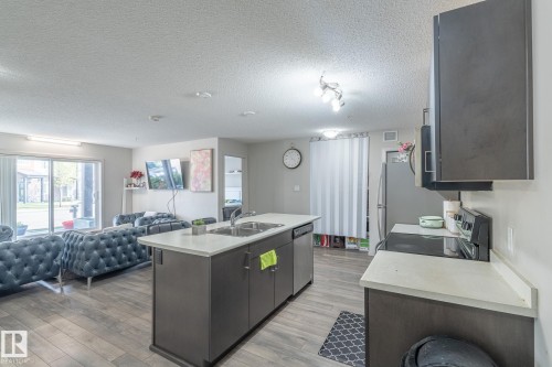 Open concept living area featuring wood-finish flooring, a kitchen island with an integrated sink and dishwasher, white countertops, and dark cabinetry - 107 142 Ebbers Boulevard, Edmonton, AB 