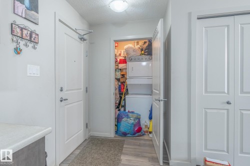 Entryway featuring wood-finish flooring, a white paneled door, and a utility closet with a stacked washer and dryer - 107 142 Ebbers Boulevard, Edmonton, AB 