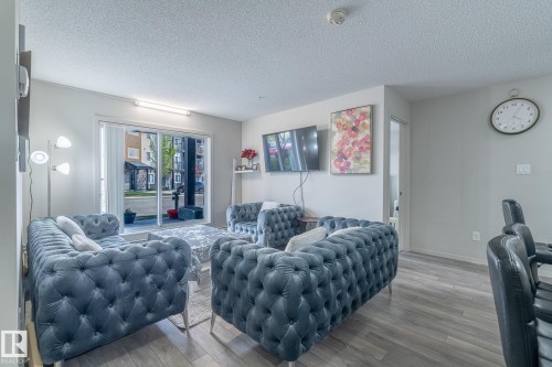 Spacious living area featuring wood-finish flooring, light grey walls, and a sliding glass door leading to an outdoor patio - 107 142 Ebbers Boulevard, Edmonton, AB 